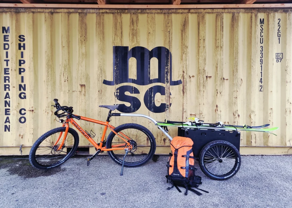 Der Wagen mit Ski am Fahrrad; daneben steht der Rucksack.