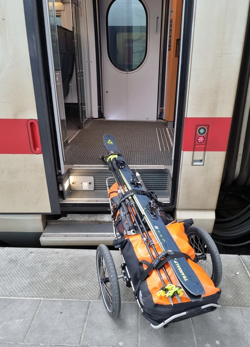 Trolley mit Ski und Gepäck vor dem Einstieg eines Zuges.